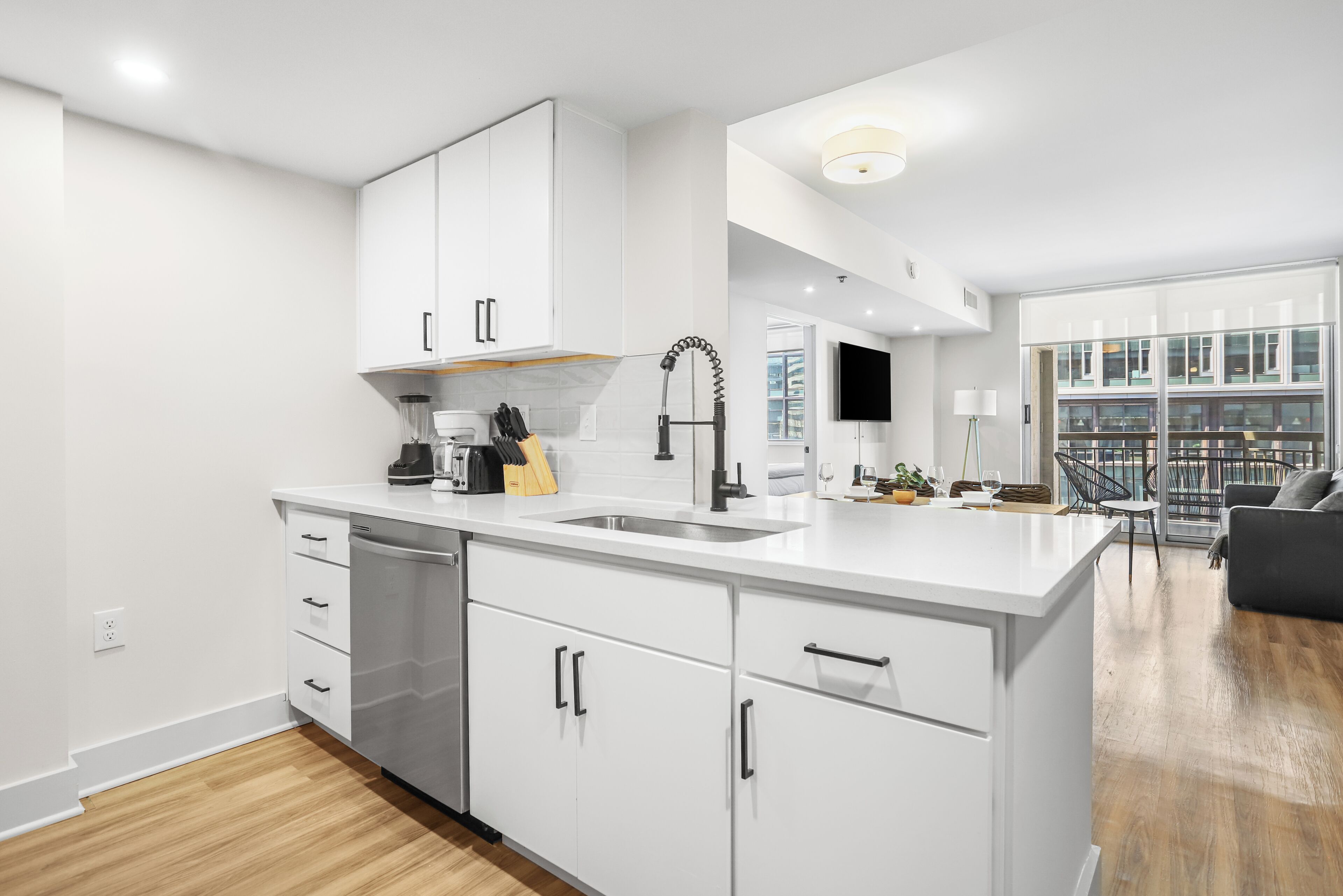 A modern kitchen with white cabinetry, a built-in dishwasher, and a large island with a sink.