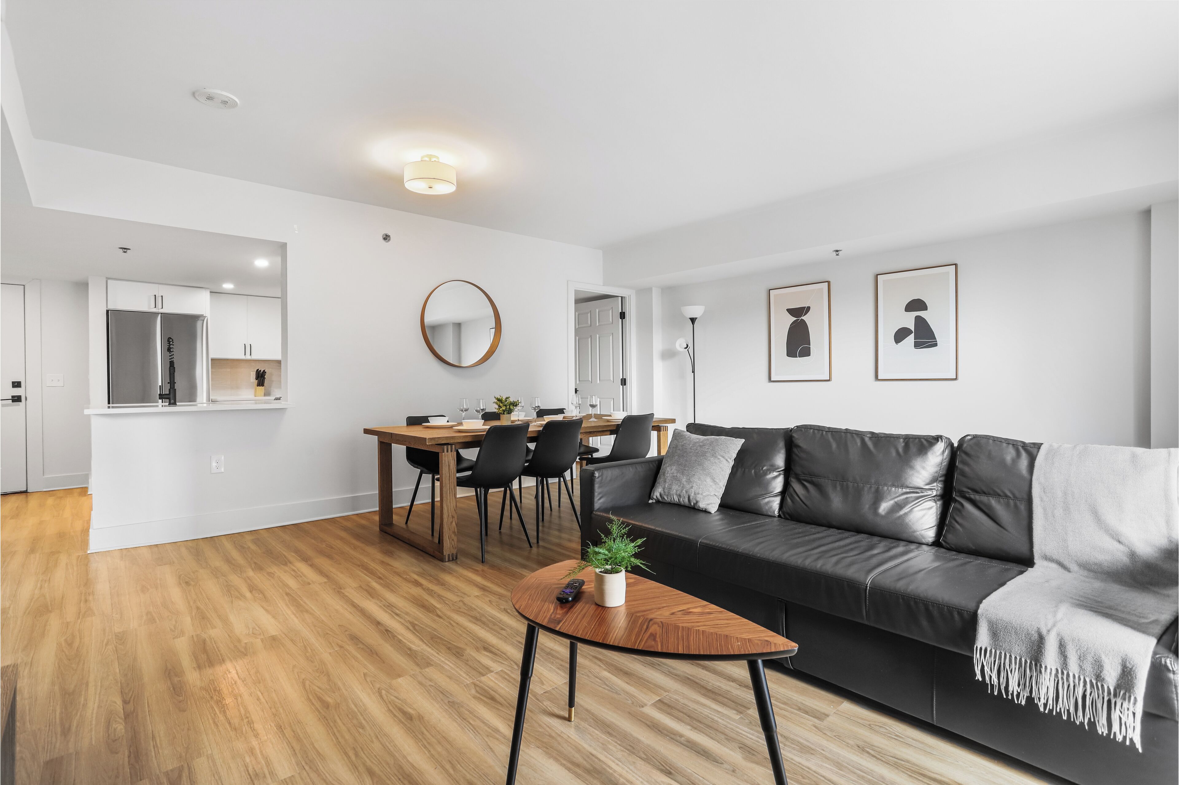En moderne stue med en sort lædersofa, et træsofabord og et spiseområde med et træbord og stole.