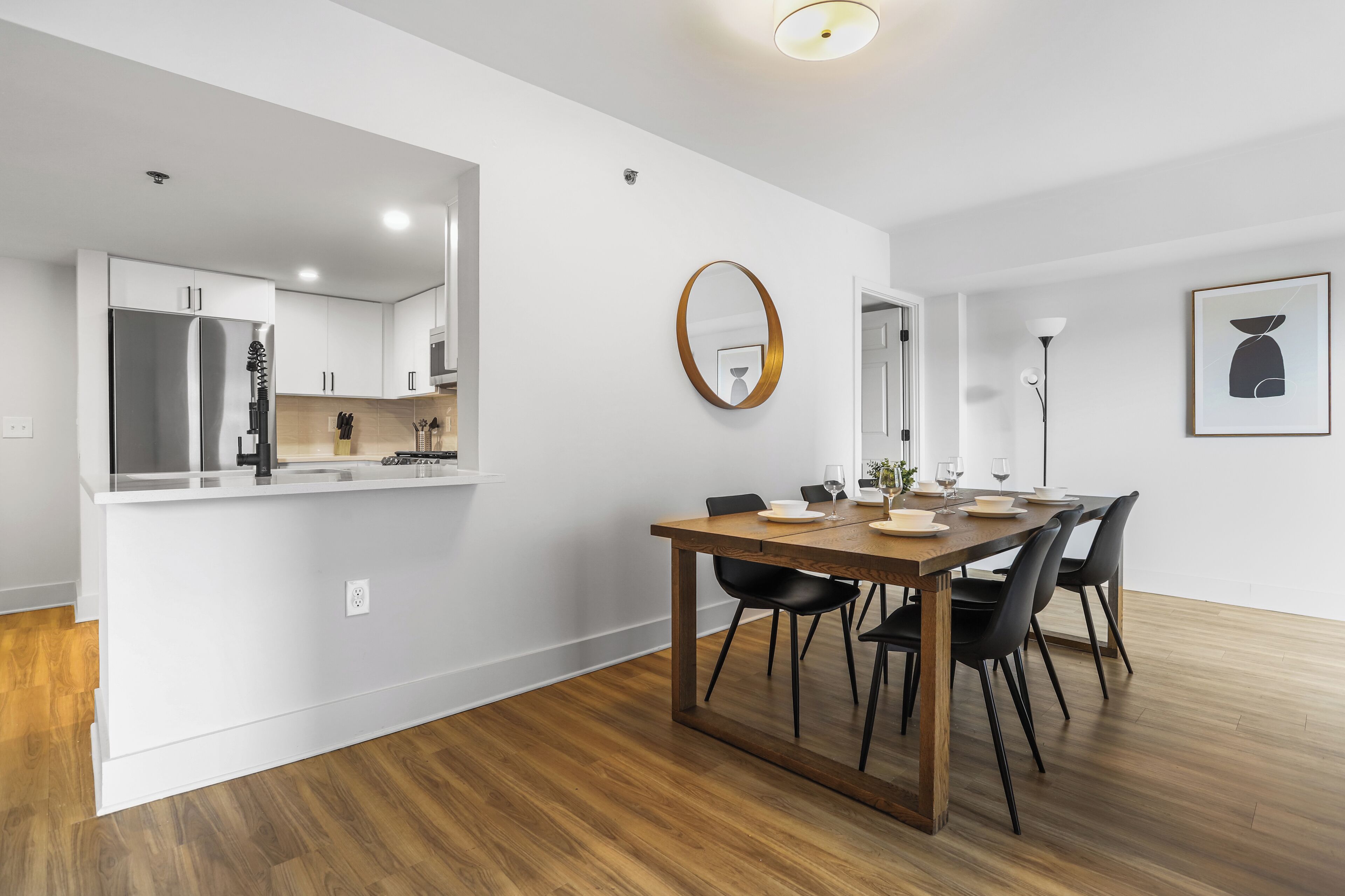 Een moderne keuken met witte kasten, een roestvrijstalen koelkast en een houten eettafel met zwarte stoelen.