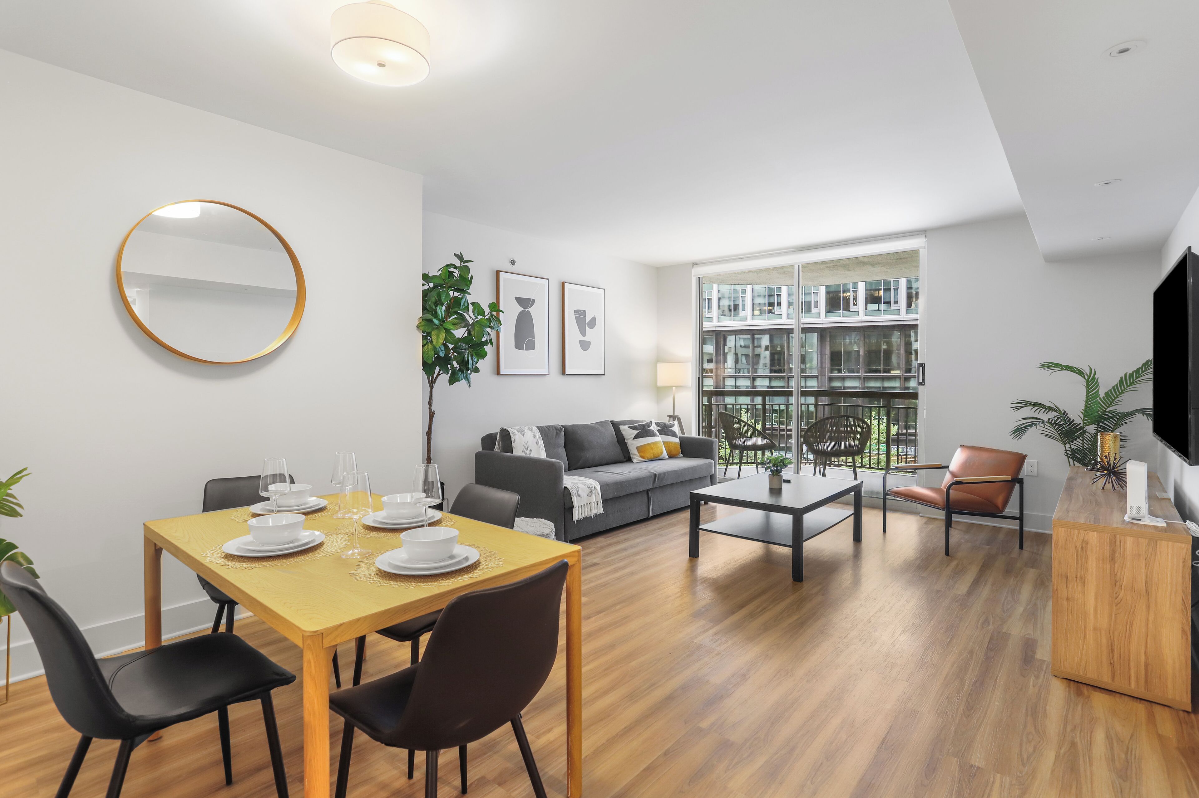 Uma sala de estar moderna com área de jantar, um sofá cinzento, uma mesa de centro e uma TV sobre um aparador de madeira.