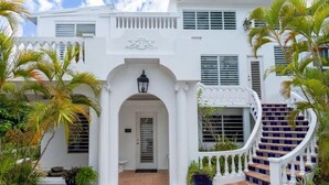 A white colonial-style building with a central entrance, a staircase with blue patterned tiles, and tropical plants.