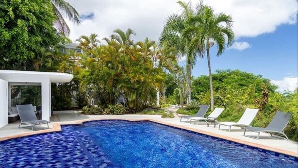 A swimming pool with a blue mosaic tile floor, surrounded by lounge chairs and palm trees.