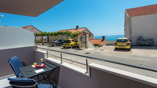 A balcony with a table and chairs, overlooking a street with parked cars and houses. - Charming 1-bedroom apartment in lovely Cavtat (Cavtat)