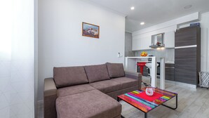 A modern living room with a brown sectional sofa, a colorful striped coffee table, and a kitchen area in the background. - Charming 1-bedroom apartment in lovely Cavtat (Cavtat)