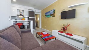 A modern living room with a sofa, a coffee table, and a TV on a white stand. - Charming 1-bedroom apartment in lovely Cavtat (Cavtat)