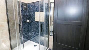 A glass-enclosed shower stall with a dark marble wall, a white floor, and a wooden door.
