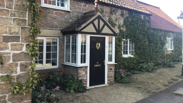A stone house with a black door, white-framed windows, and a tiled roof. - Rose Cottage (Nottingham)