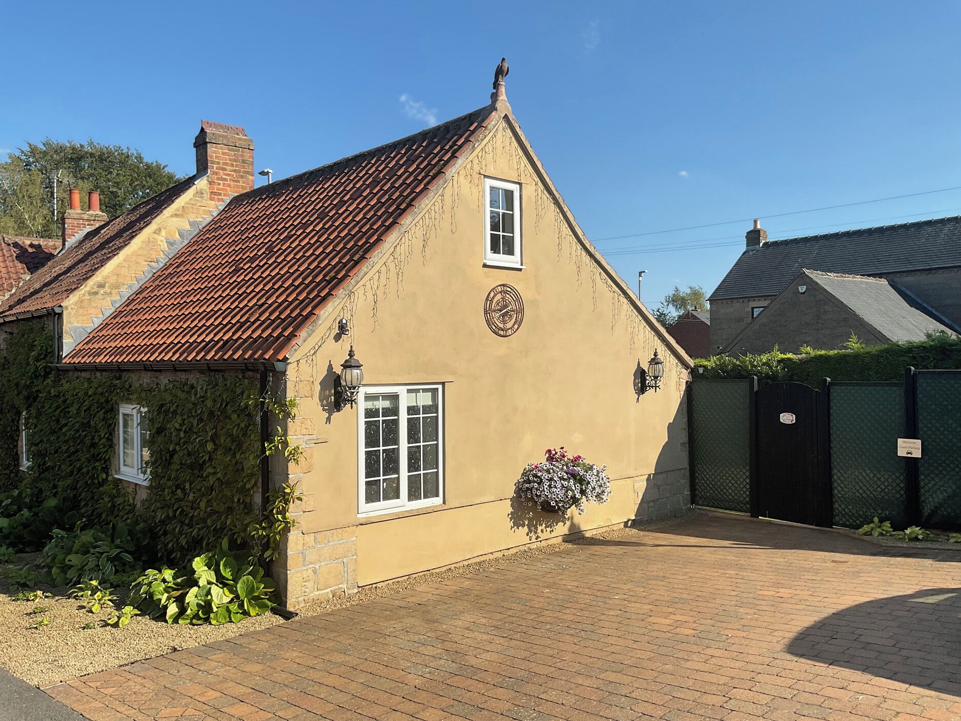 A small, single-story building with a tiled roof, a brick chimney, and a small garden area with plants and flowers.