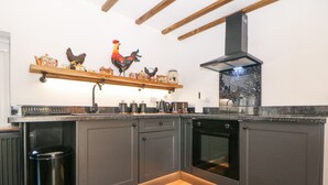A modern kitchen with dark cabinets, a wooden floor, a built-in oven, and a black trash bin. - Rose Cottage (Nottingham)