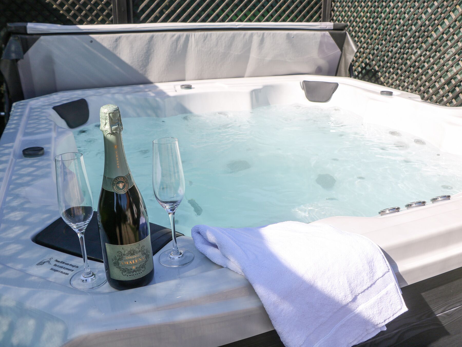 A hot tub with a bottle of champagne and two glasses on a table.