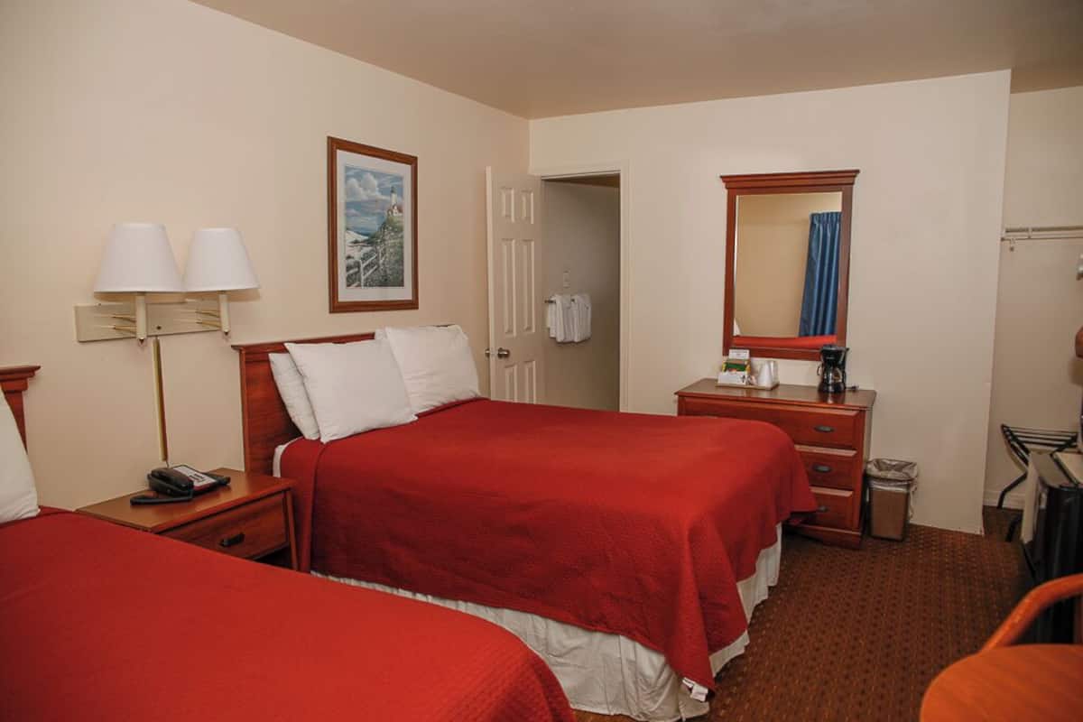 A hotel room with two beds, a desk with a mirror, a lamp, and a painting on the wall.