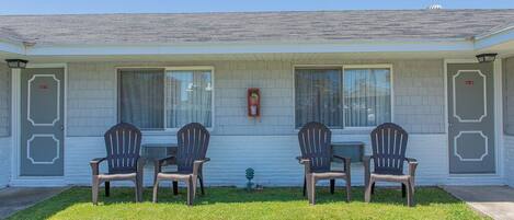 A motel with four Adirondack chairs in front, a fire hydrant, and a small garden area.