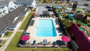 En rektangulär swimmingpool med en omgivande terrass, solstolar och parasoller.