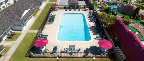 A rectangular swimming pool with a surrounding deck, lounge chairs, and umbrellas.