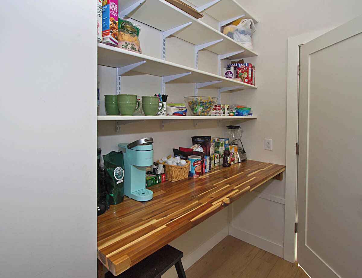 Una cocina con estantes blancos, una encimera de madera y diversos utensilios de cocina.