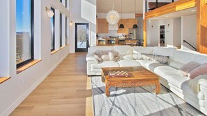 Ein geräumiger Wohnbereich mit einem großen weißen Sofa, einem Holztisch und Blick auf die Küche und den Essbereich.