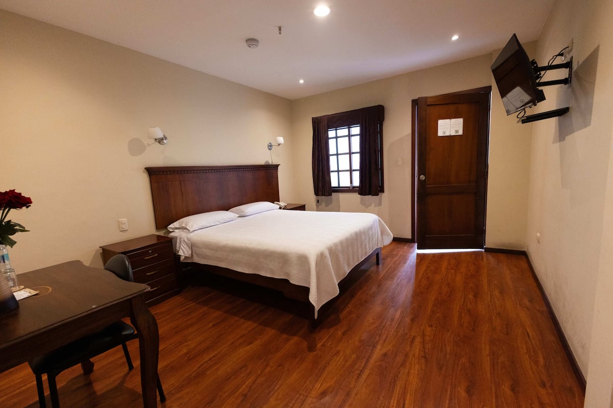 A bedroom with a wooden bed, a desk, a chair, a dresser, and a window with curtains.