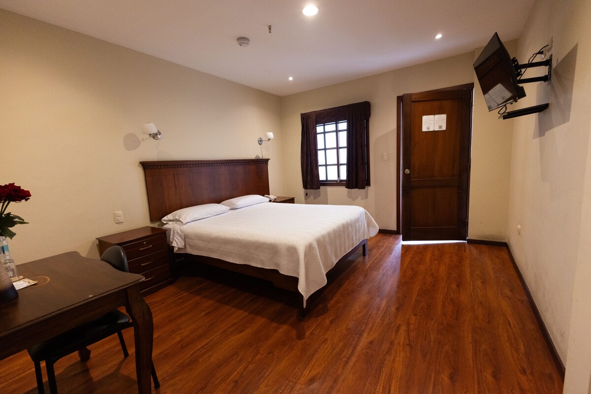 Un dormitorio con una cama de madera, un escritorio, una silla, un aparador y una ventana con cortinas.