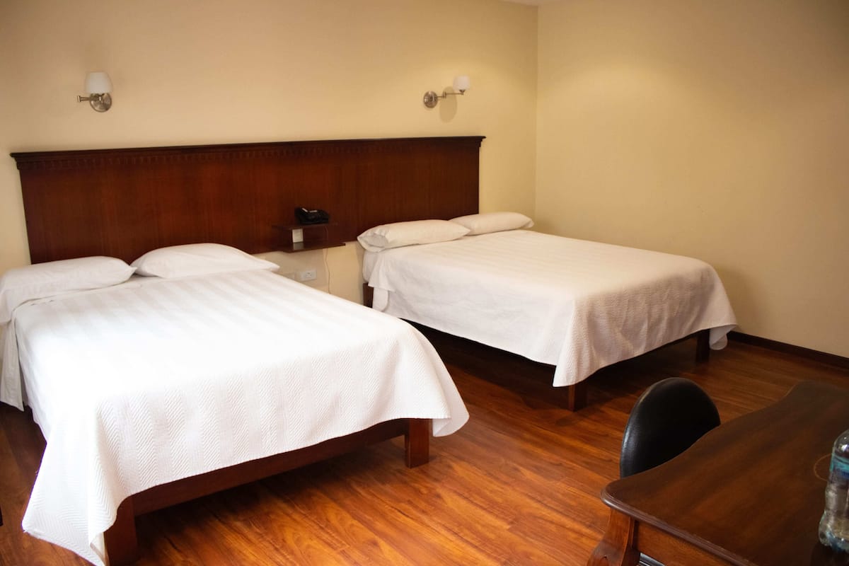 Two single beds with wooden headboards, a wooden table, and a chair in a hotel room.