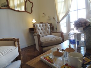 Une pièce comprenant un fauteuil capitonné, une table en bois sur laquelle se trouve un plateau de collations, une bouteille d’eau et une tasse.
