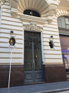 Fachada de edifício com uma grande porta metálica preta ornamentada, molduras decorativas e uma pequena janela acima da porta.