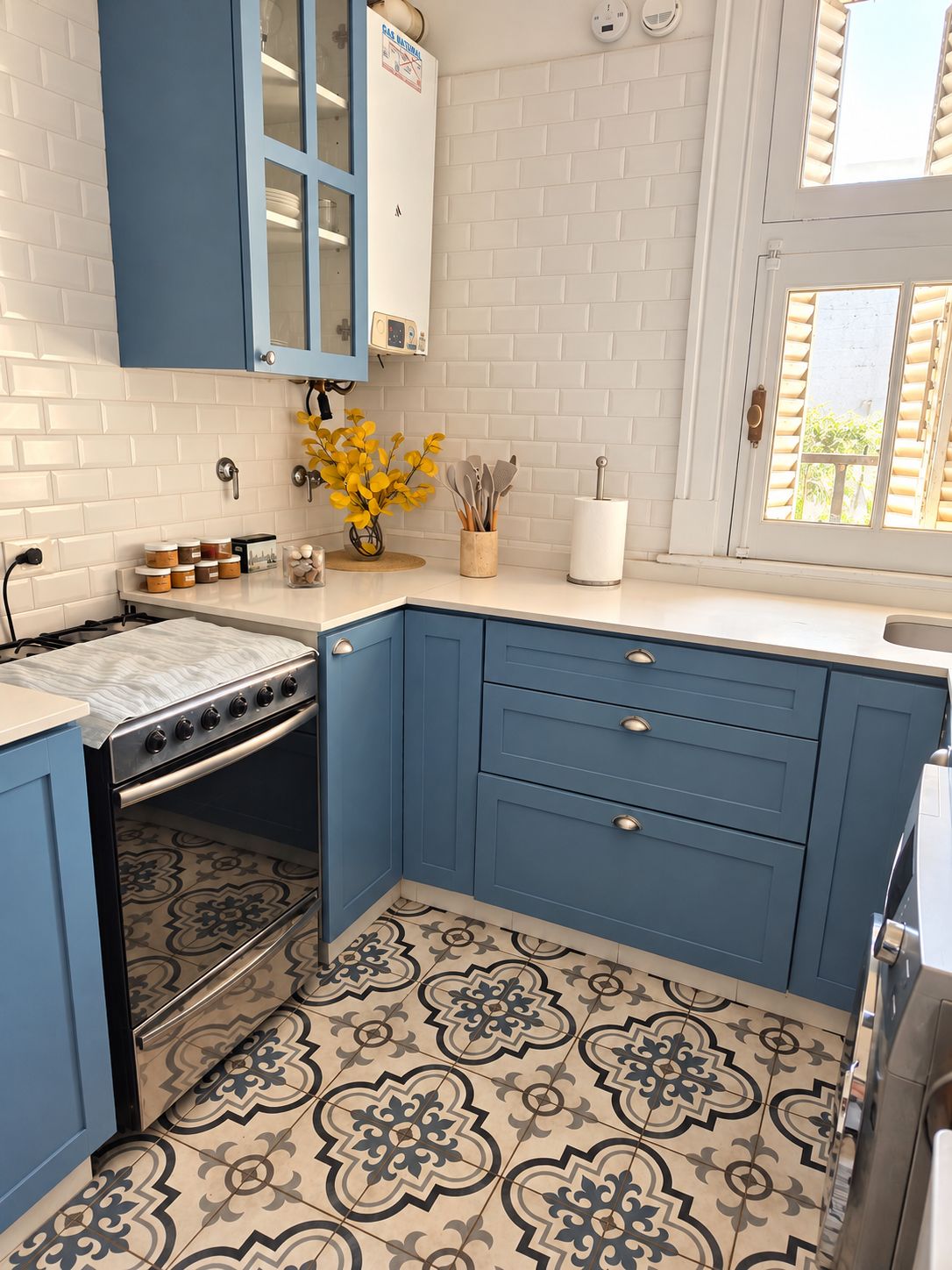 A kitchen with blue cabinets, a patterned floor, and a window with shutters.