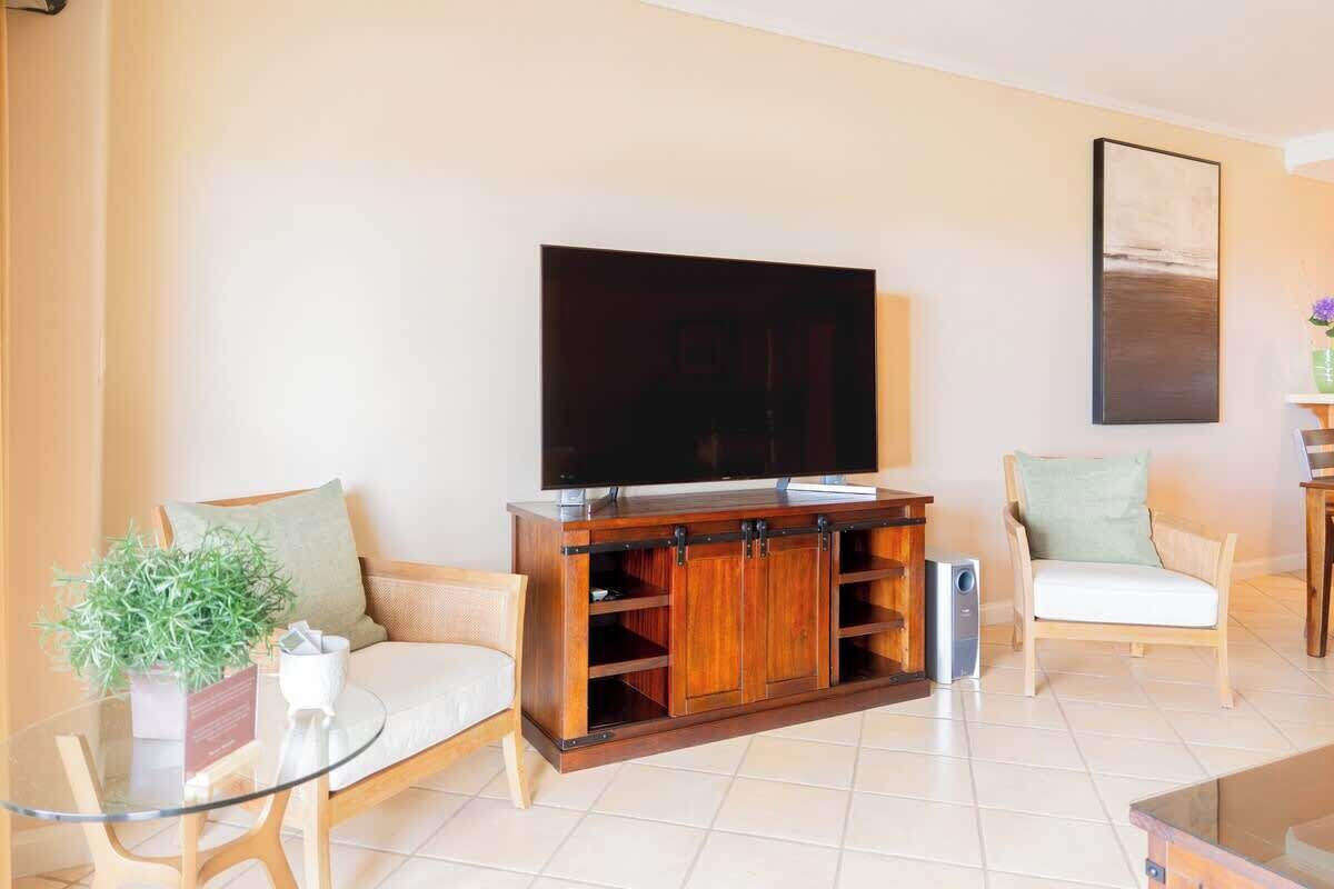 A living room with a sofa, a glass coffee table, a TV on a wooden cabinet, and a chair.