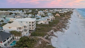 Un quartier résidentiel situé sur la côte, avec des propriétés donnant sur la plage, notamment une grande maison avec piscine et un bâtiment plus petit doté d’un balcon.