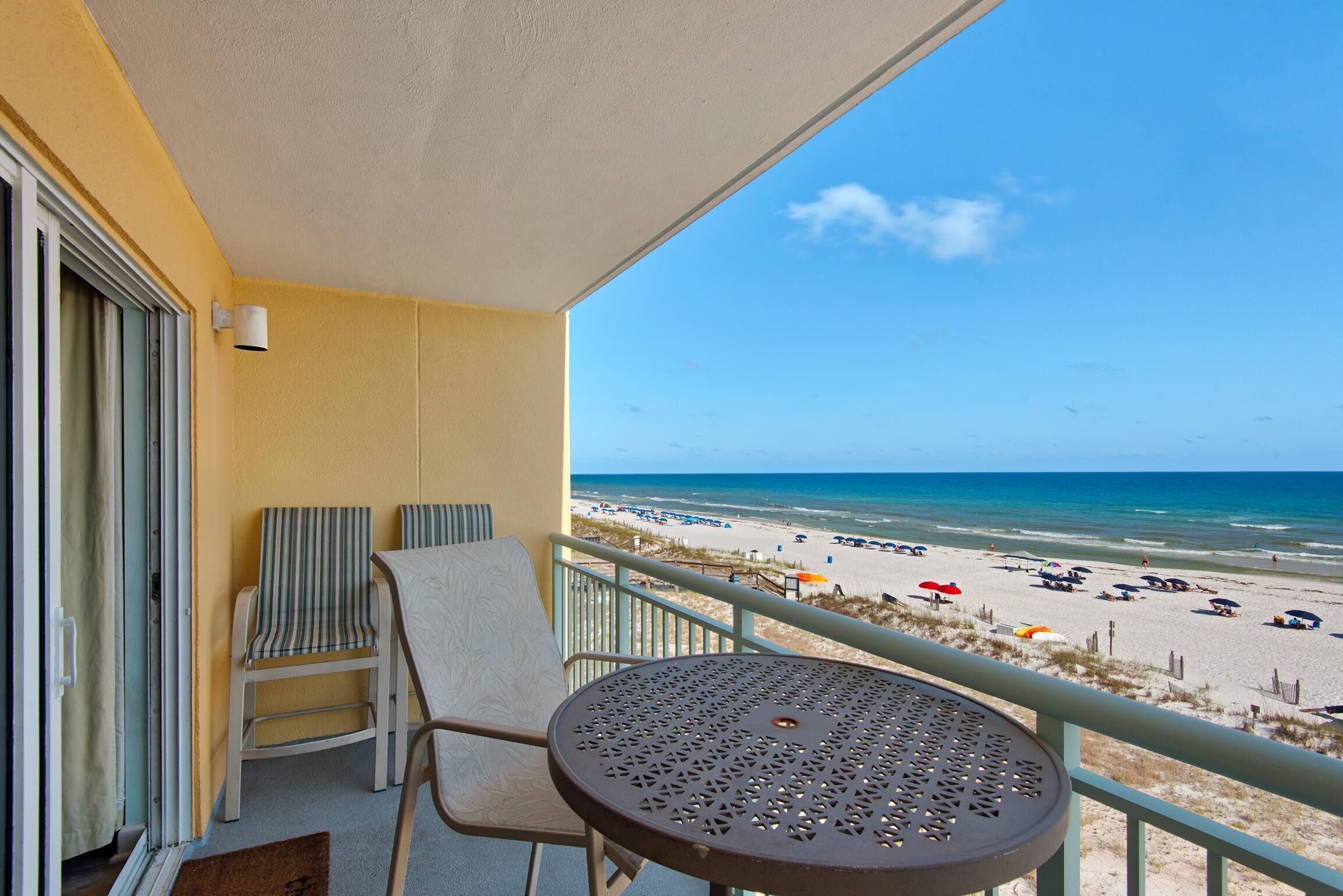 A balcony with a view of the beach, a chair, a table, and a door with a curtain.
