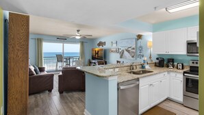A kitchen with a view of the ocean, a dining area with a view, and a living room with a sofa and chairs. - Pelican Isle 411 (Fort Walton Beach)