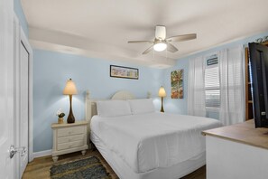 A bedroom with a bed, nightstands, a ceiling fan, and artwork on the walls.