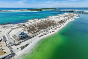 An aerial view of a coastal area with a pier extending into the water, a sandy beach, and a building with a blue roof near the shore.