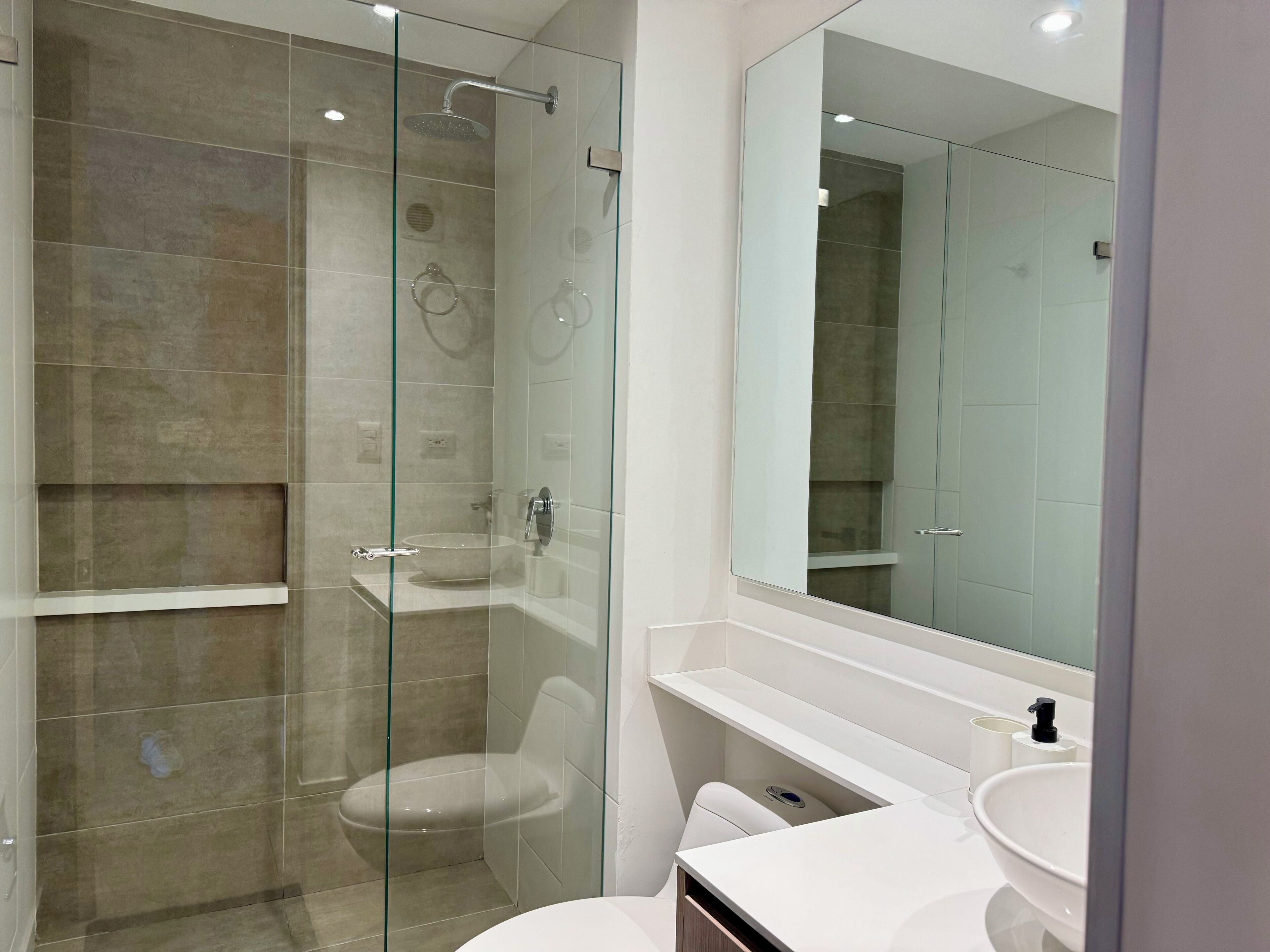 A modern bathroom with a glass-enclosed shower, a white sink, and a large mirror.