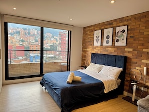 Une chambre à coucher moderne avec une grande fenêtre, un mur d’accent en briques et un lit doté d’une tête de lit bleue.