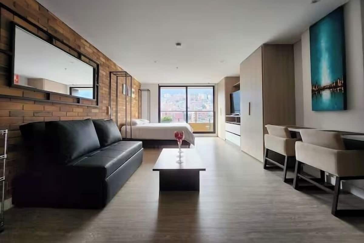 Ein modernes Wohnzimmer mit einem schwarzen Ledersofa, einem Couchtisch mit einem Weinglas, einem Fernseher und einem großen Fenster mit Blick auf die Stadt.