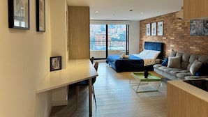 A modern apartment with a large window, a bed, a sofa, a desk, and a dining area.