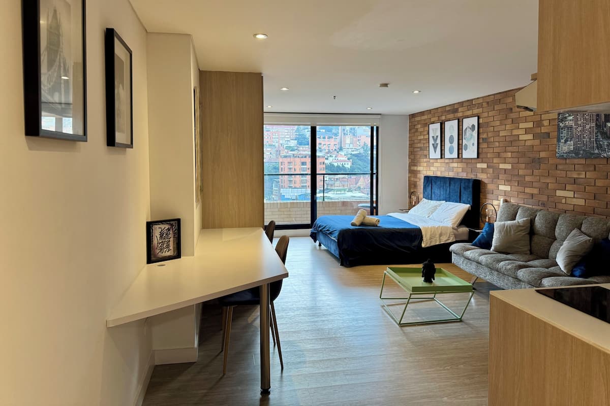 Eine moderne Wohnung mit großem Fenster, einem Bett, einem Sofa, einem Schreibtisch und einem Essbereich.