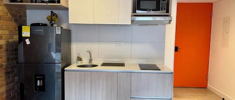 A compact kitchen with a refrigerator, microwave, sink, and cabinets.
