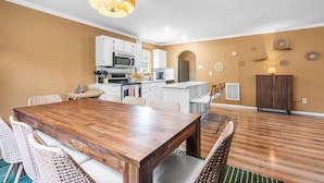 A modern kitchen with white cabinets, a wooden dining table, wicker chairs, and a hanging light fixture.
