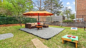 An outdoor patio area with a wicker sofa set, a round coffee table, and a small table with a board game.