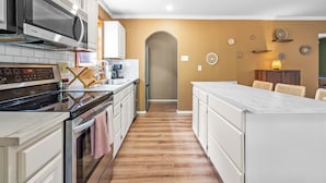 A modern kitchen with white cabinetry, a stainless steel range hood, and a wooden floor.