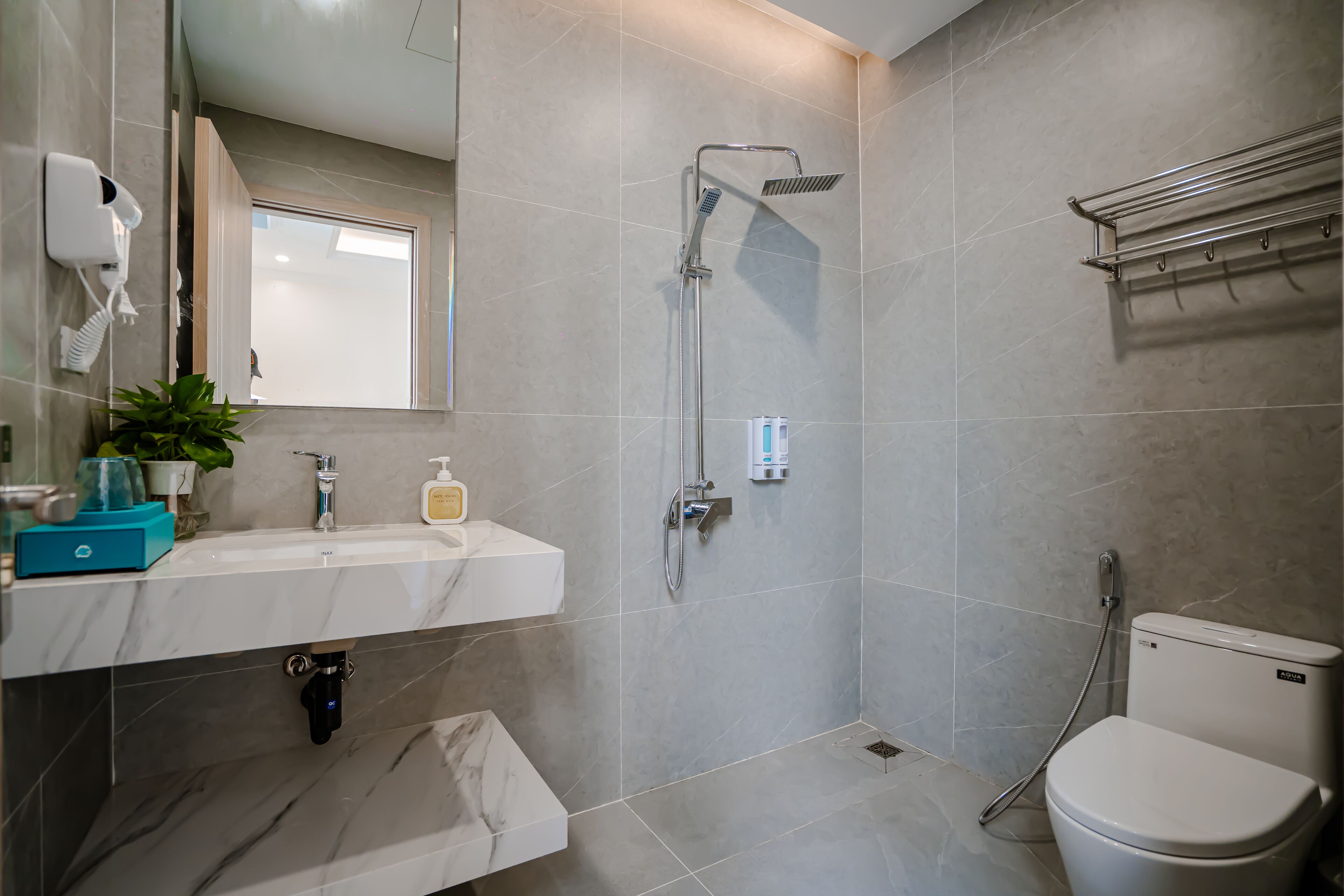 Une salle de bain moderne avec un lavabo blanc, un miroir, une douchette à main, des toilettes et un porte-serviettes.