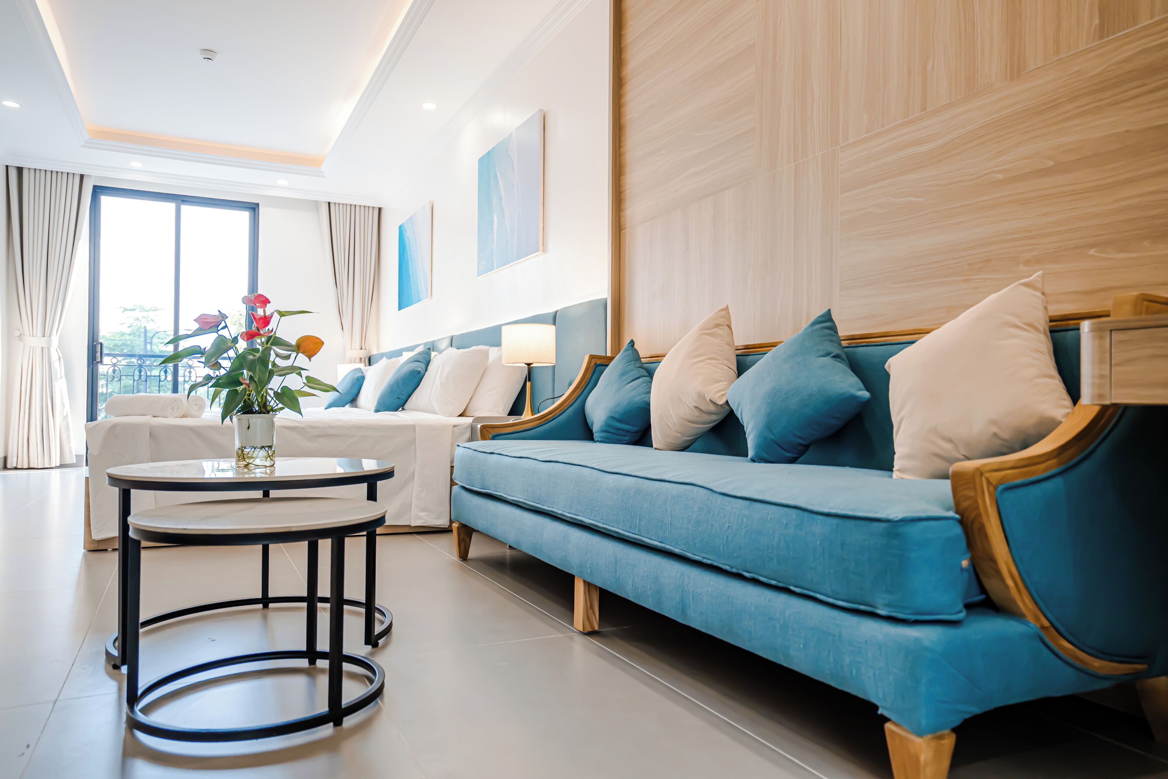 Una sala de estar moderna con un sofá azul, un sillón blanco y una mesa redonda con un jarrón de flores.