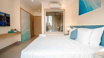 A hotel room with a large bed, a TV, a mirror, and a view of the city through the window.