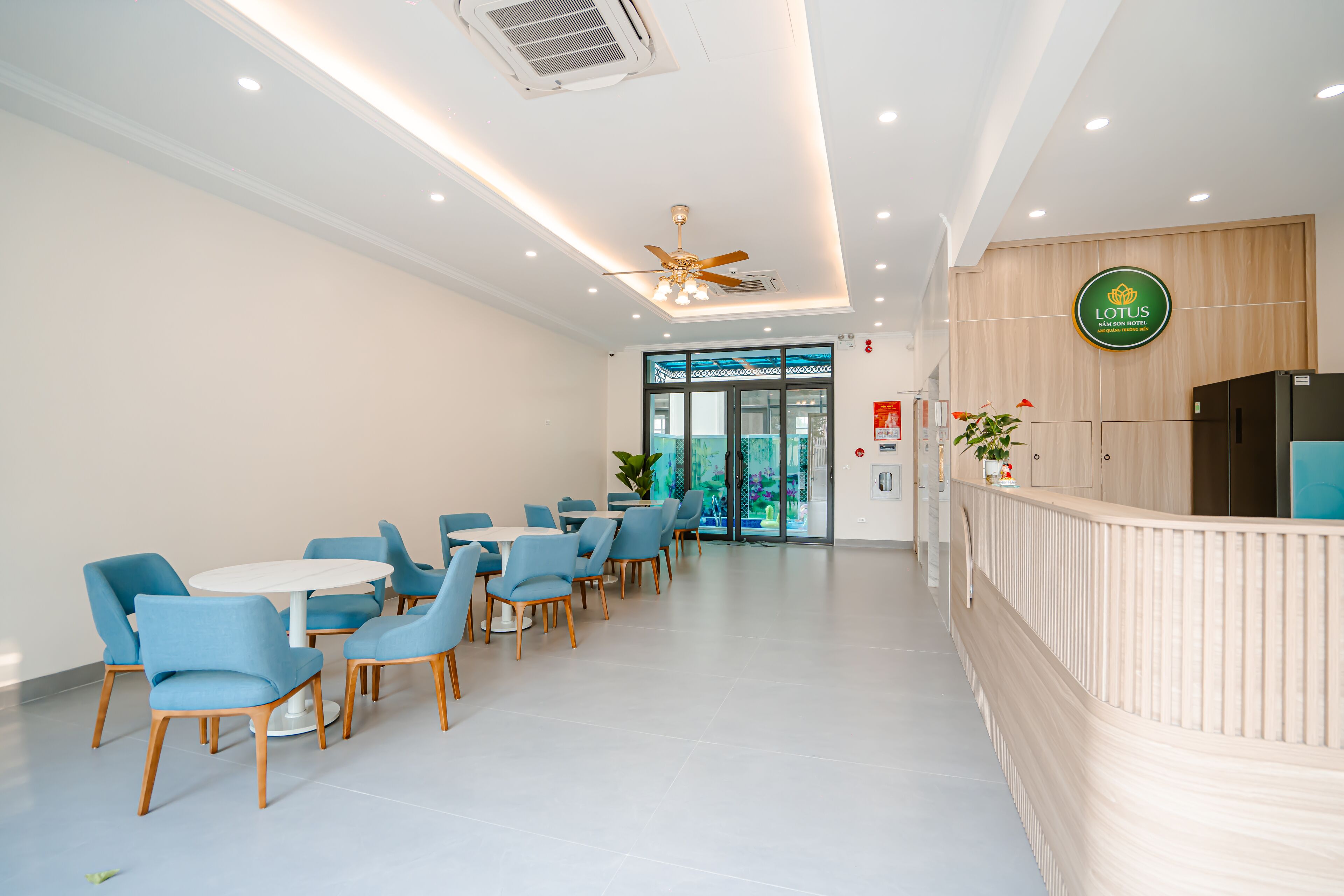 A modern reception area with a wooden reception desk, a ceiling fan, and a large window with a view of the outdoors.