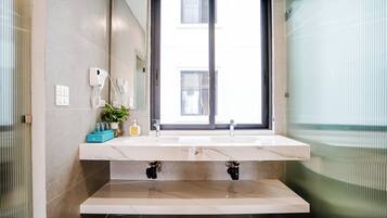 Een badkamer met een groot raam, een witte wastafel en een spiegel.