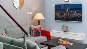A modern living room with a sofa, a coffee table, a lamp, a wall-mounted TV, and a cityscape painting. - Coastal Escape in Tower Isle BeachNearby (Tower Isle)