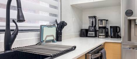 Una cocina moderna con un grifo negro, cafetera, licuadora y tostadora.