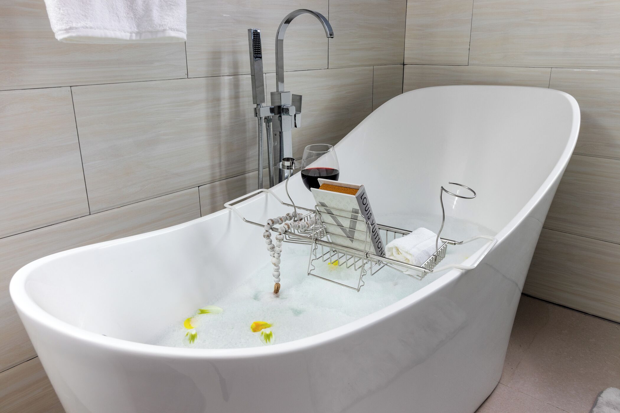 A modern bathroom with a freestanding bathtub, a handheld showerhead, and a glass of red wine.