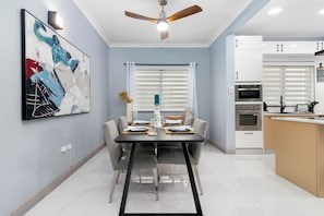 A modern dining area with a black table, white chairs, and a ceiling fan. - Coastal Escape in Tower Isle BeachNearby (Tower Isle)